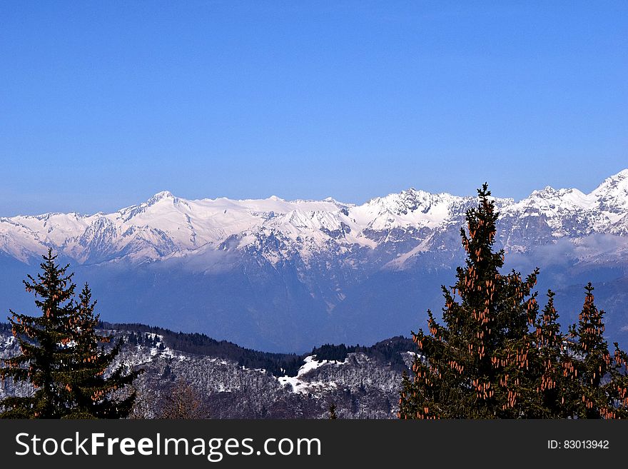 Landscape of snow covered mountain peaks over forest in valley against blue skies on sunny day. Landscape of snow covered mountain peaks over forest in valley against blue skies on sunny day.