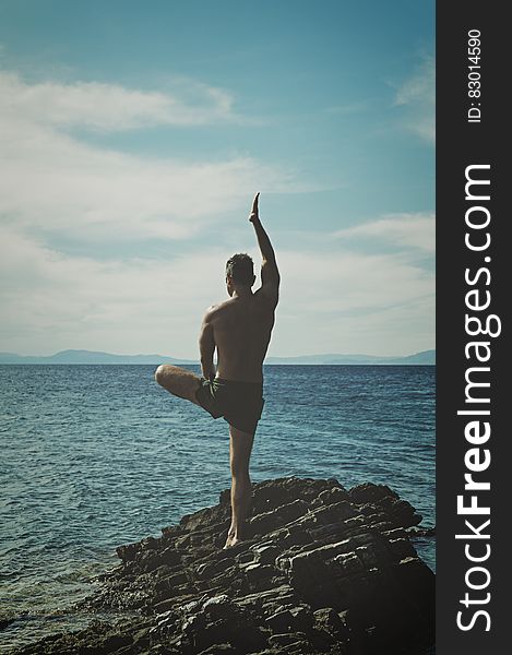Topless Man Standing on Rock Formation Using Right Leg Only