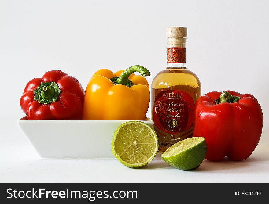 Red and Green Bell Pepper Inside White Ceramic Tray Near to Bottle and Lemon