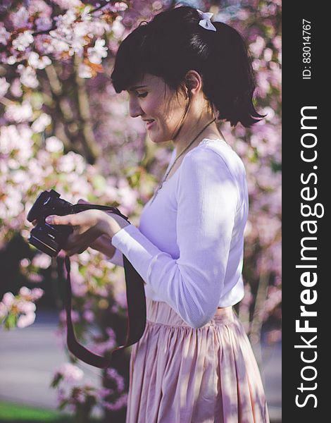 Woman in White Long Sleeve Top and Pink Skirt Holding Black Dslr Camera