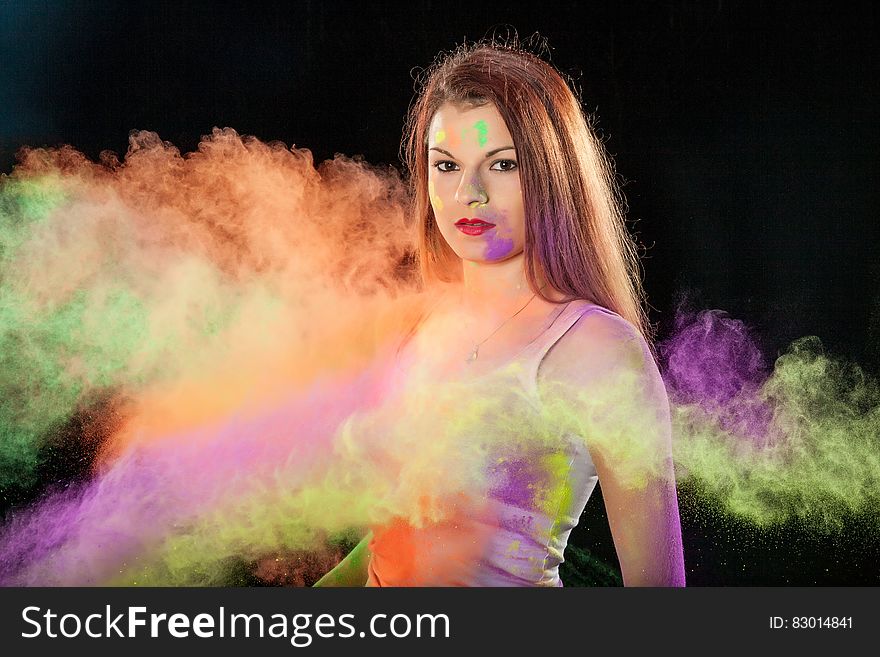 Portrait of brunette woman with purple and green smudges standing in colorful smoke. Portrait of brunette woman with purple and green smudges standing in colorful smoke.