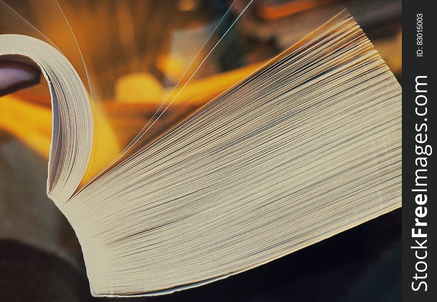 Unseen person leafing through a very thick book with binding visible, golden background.