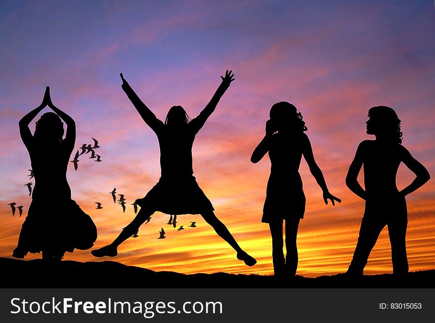 Silhouette of 4 Women With the Background of Birds Flying Under Yellow and Grey Sky