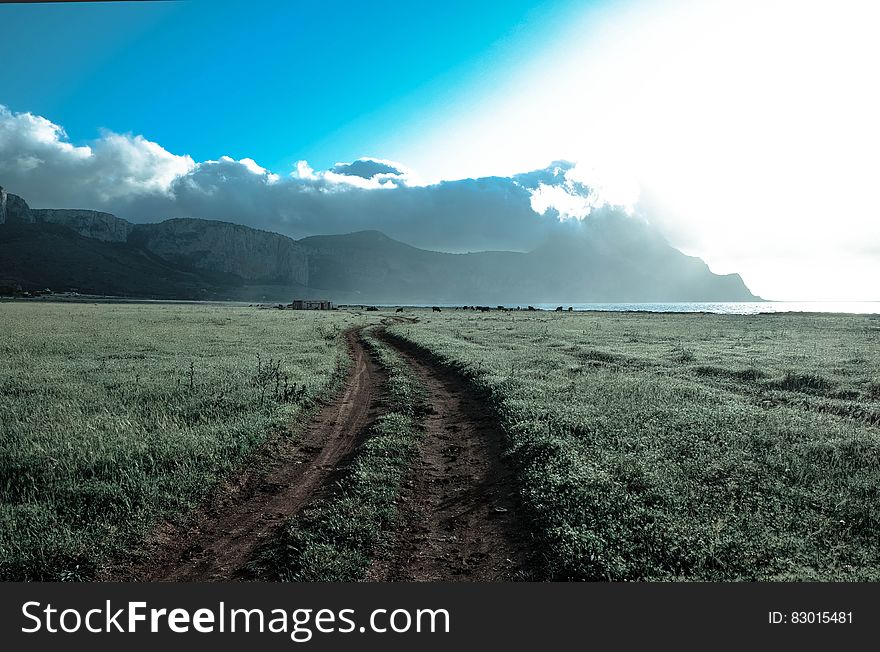 Green Grass Field Beside Brown Mountains Under White Cloudy Sky