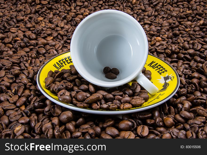 White Ceramic Cup on Yellow Plate With Coffee Beans