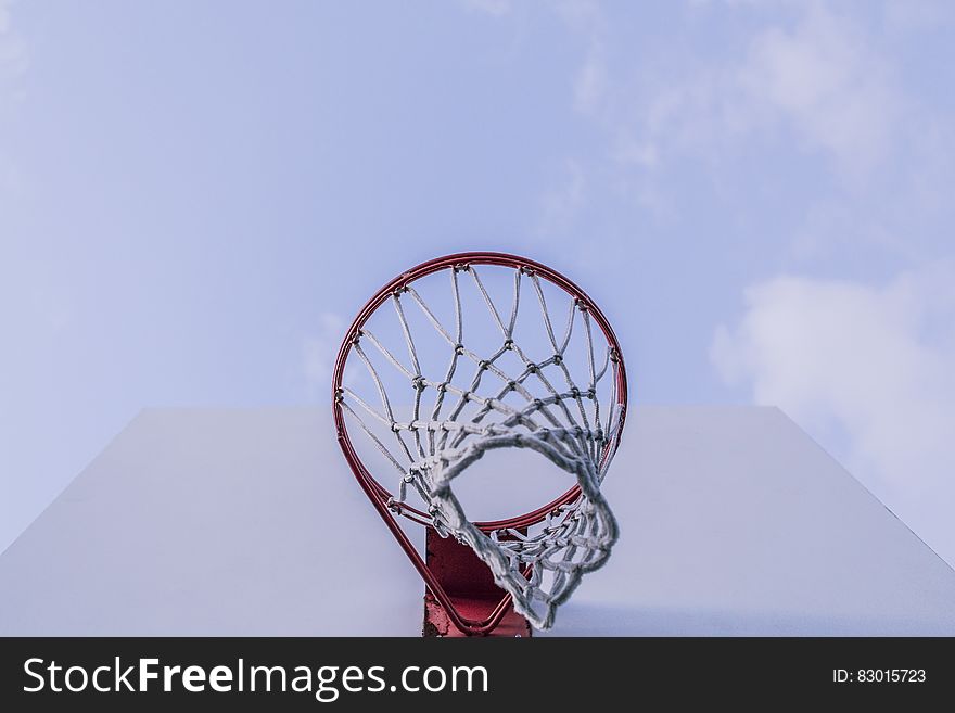 Basketball net on rim on white backboard against blue skies.