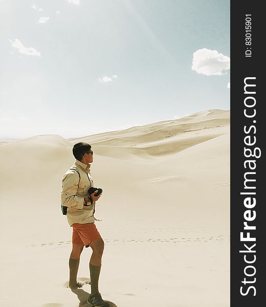 A photographer standing in a sandy African desert watching the dunes. A photographer standing in a sandy African desert watching the dunes.