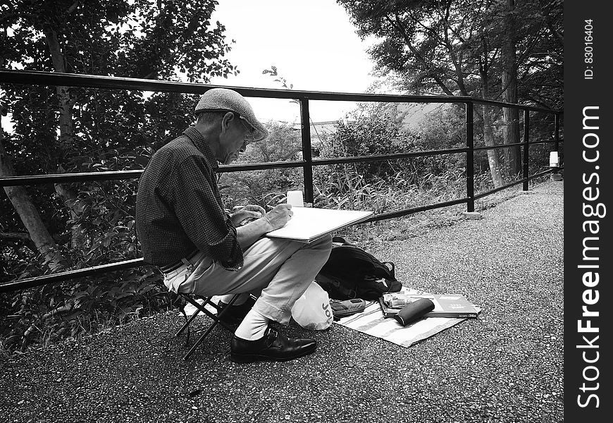 A man sketching next to a railing in the forest.