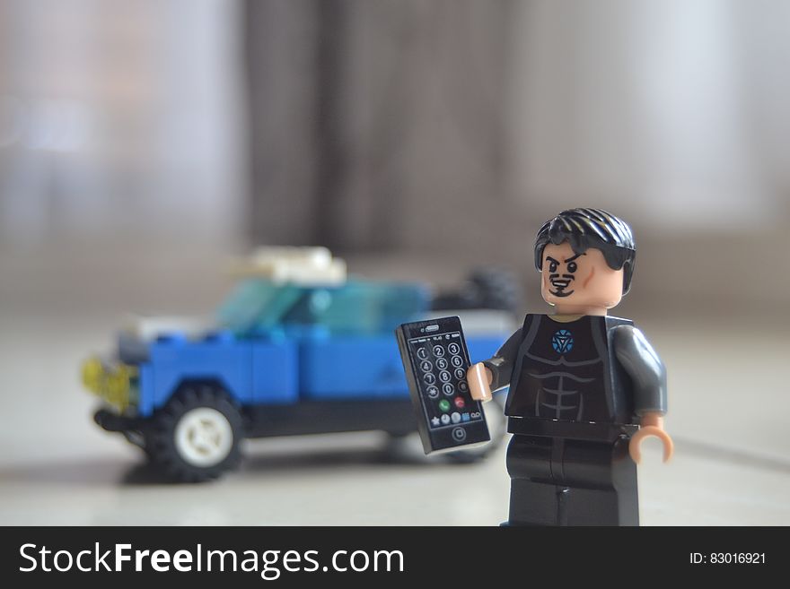 Lego construction with 4 by 4 blue jeep and mini character (possibly policeman) holding a black electronic device. Lego construction with 4 by 4 blue jeep and mini character (possibly policeman) holding a black electronic device.