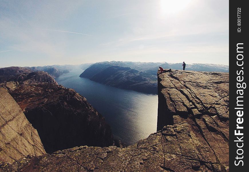 Person standing on edge of rocky precipice over river on sunny day. Person standing on edge of rocky precipice over river on sunny day.