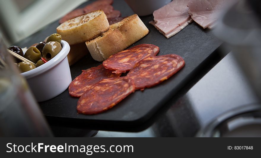 Tray of appetizing foods including green olives, bread, ham and salami.