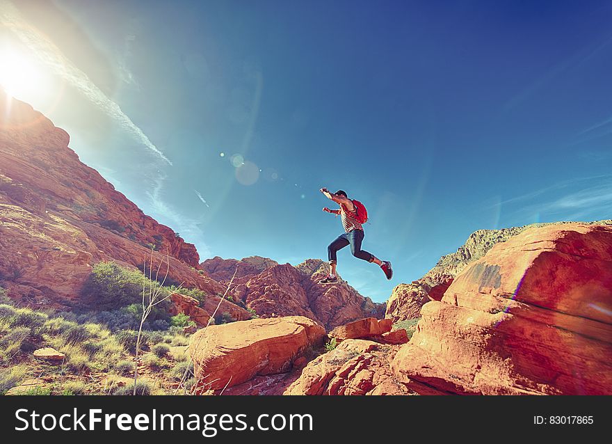 Man with backpack jumping over rocks in desert landscape on sunny day. Man with backpack jumping over rocks in desert landscape on sunny day.