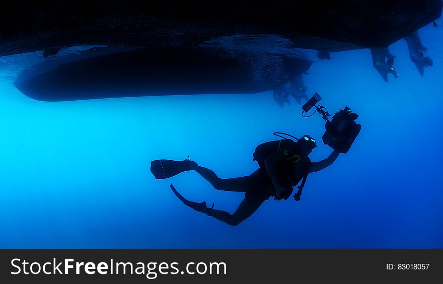 Scuba diver with equipment under ship in blue waters. Scuba diver with equipment under ship in blue waters.