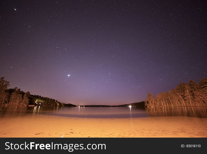 Stars in night skies over sandy beach on waterfront.