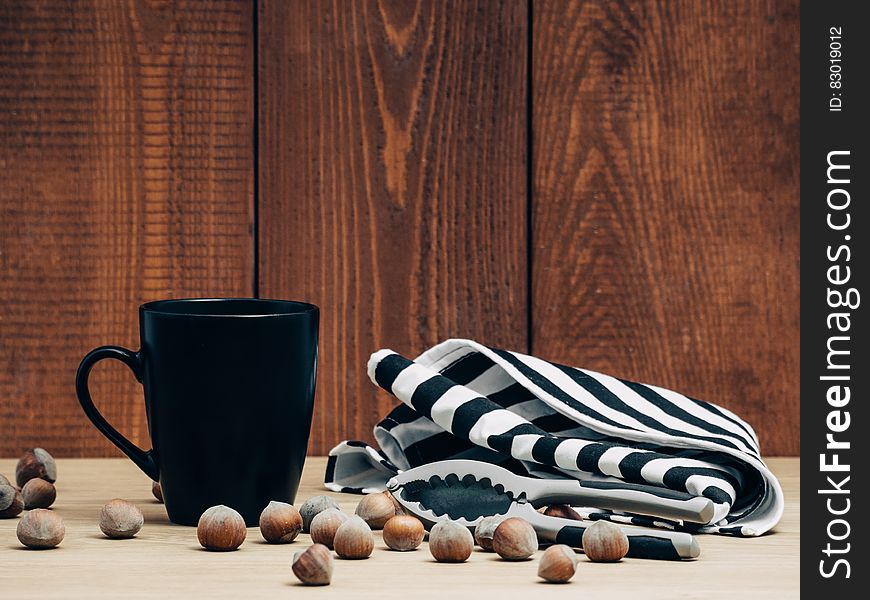 Still life of whole hazelnuts and cracker with black mug and towel against boards. Still life of whole hazelnuts and cracker with black mug and towel against boards.