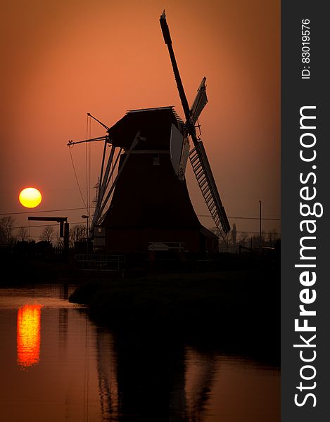 A silhouette of a Dutch windmill by water at sunset. A silhouette of a Dutch windmill by water at sunset.