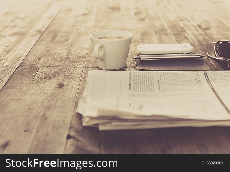 Newspaper And White Ceramic Cup On Brown Wooden Table