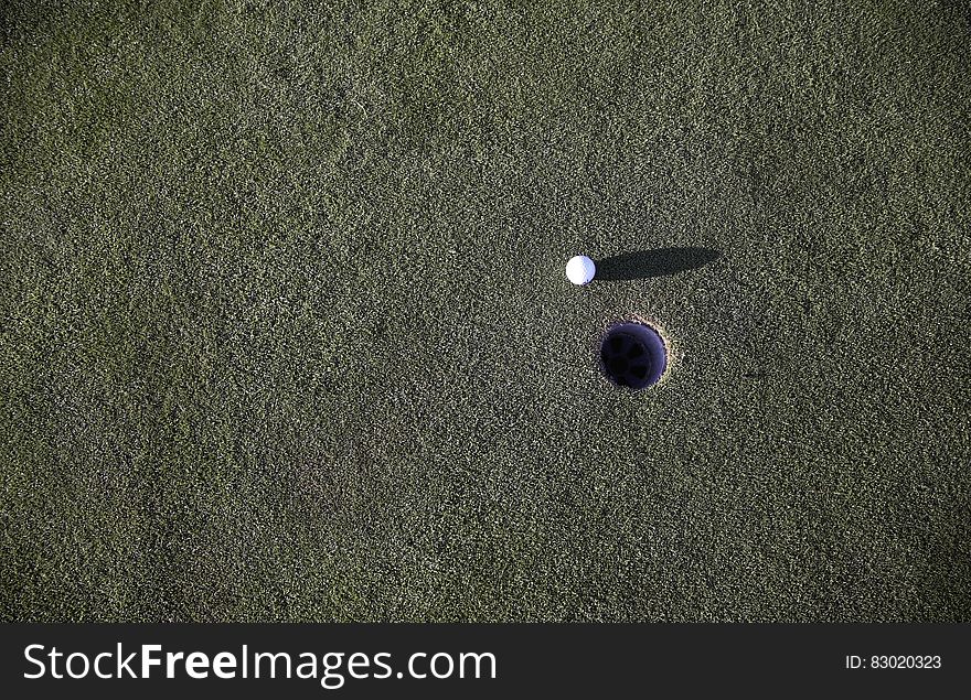 A golf ball next to the hole on a golf course. A golf ball next to the hole on a golf course.