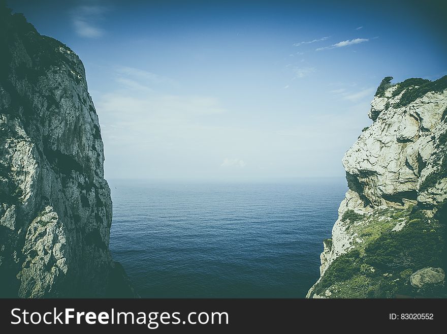 Steep rocky cliffs on coastline with blue sea and cloudscape.