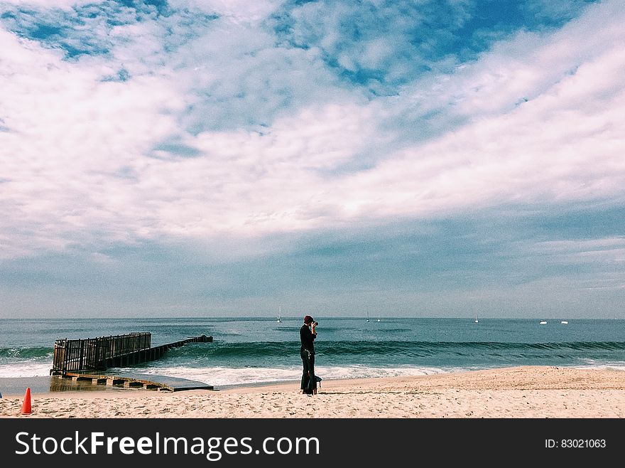 Person in Black Top Standing on Seashore Under White Clouds