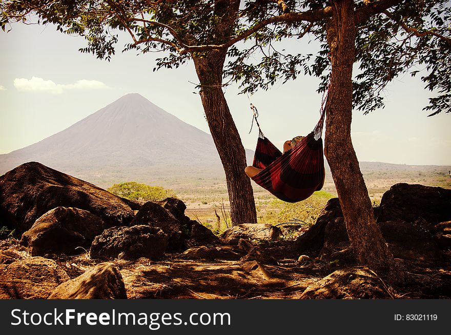 Person Lying on Black and Red Hammock Beside Mountain Under White Cloudy Sky during Daytime