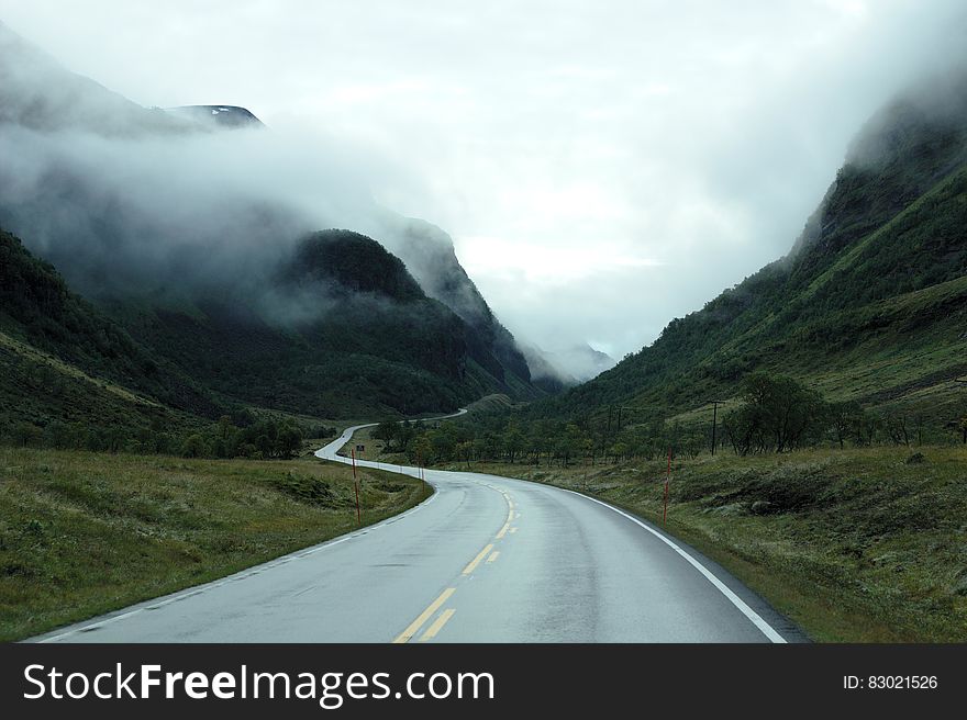 Empty winding roadway through green hillside of mountains in fog. Empty winding roadway through green hillside of mountains in fog.