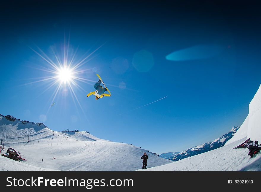 Snowboarder jumping on snowy slopes against blue skies on sunny day.