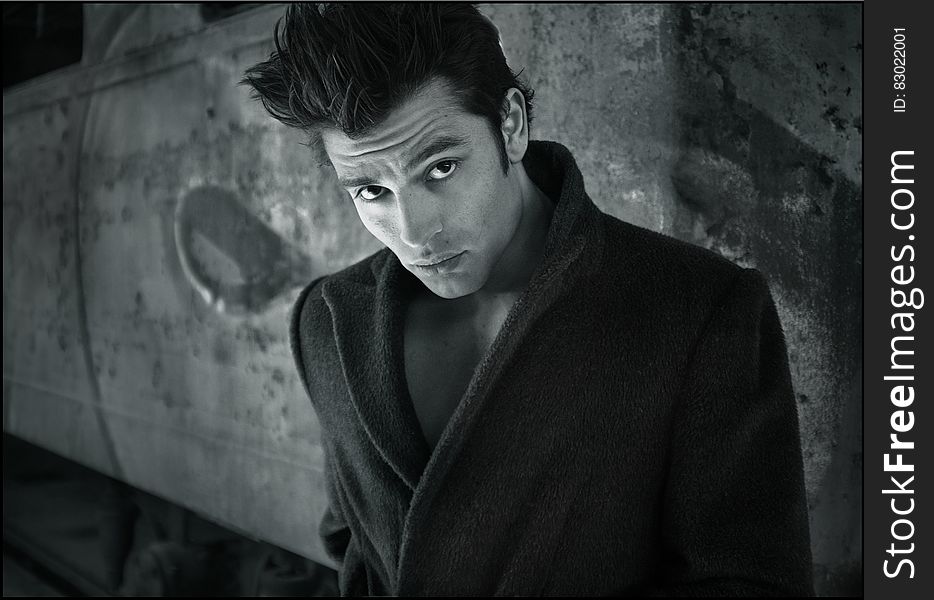 A male model posing in front of a wall in black and white.