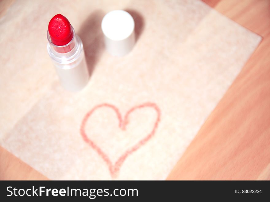 White mat on wooden table with red lipstick uncapped and a red (pink) heart drawn on the mat. Just a hint of love for Saint Valentine's day. White mat on wooden table with red lipstick uncapped and a red (pink) heart drawn on the mat. Just a hint of love for Saint Valentine's day.