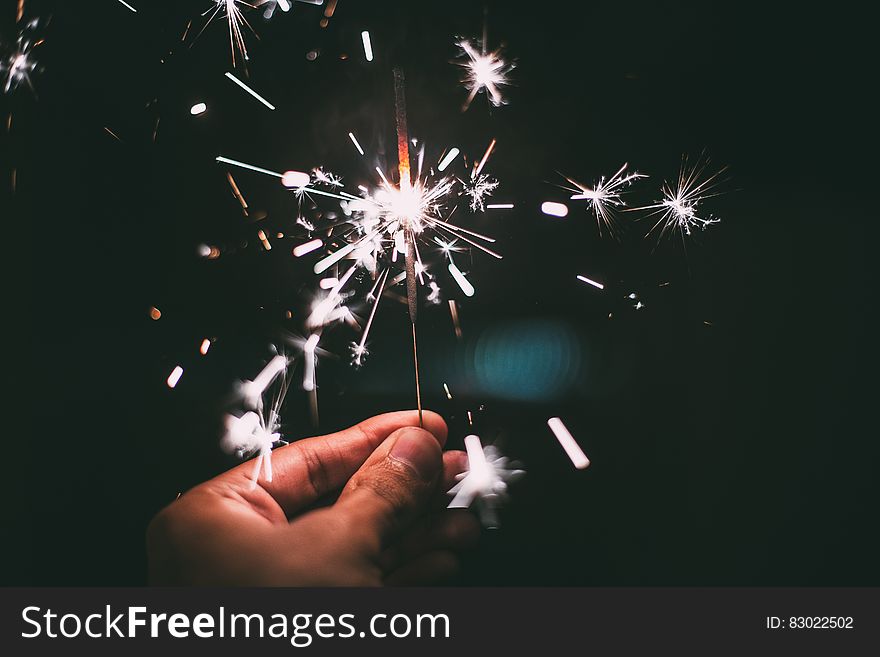 Close up of hand holding lit white sparkler against black. Close up of hand holding lit white sparkler against black.