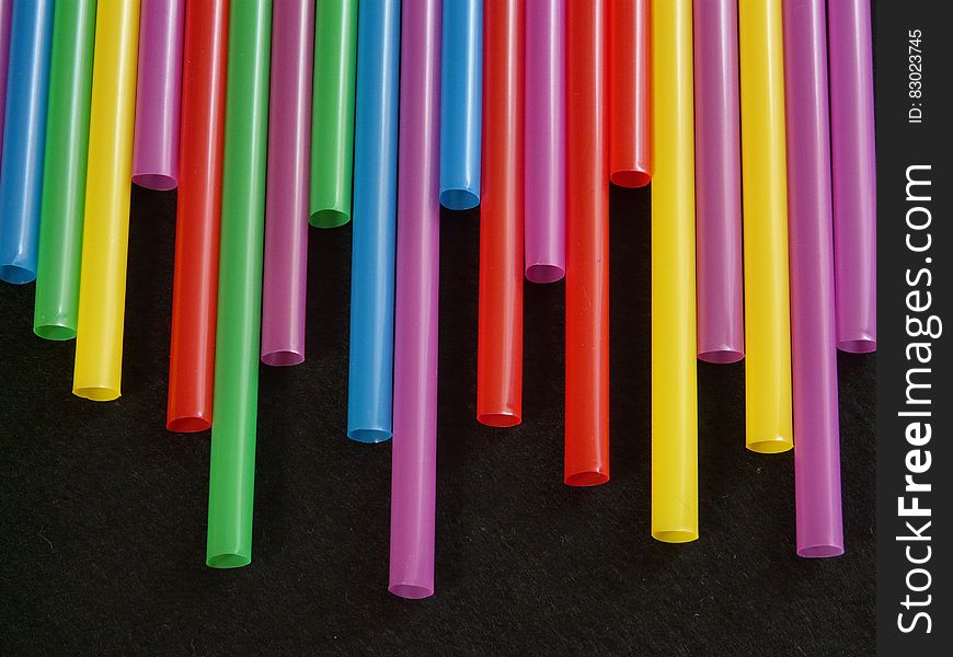 Close up of uneven line of colorful drinking straws on black.