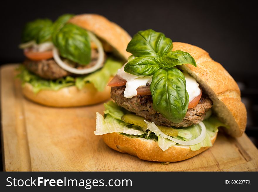 Hamburger sandwiches with lettuce, tomato, onion, pickles, mozzarella cheese and basil on kaiser rolls on wooden cutting board. Hamburger sandwiches with lettuce, tomato, onion, pickles, mozzarella cheese and basil on kaiser rolls on wooden cutting board.