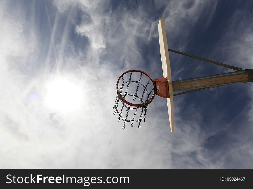 Basketball hoop on rim under backboard against blue skies with clouds on sunny day.