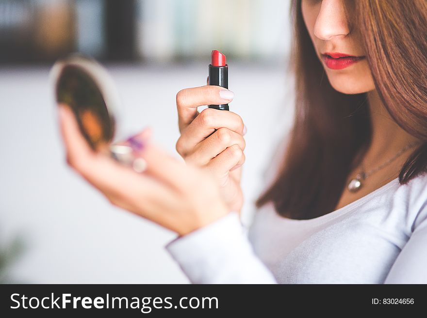 Woman with brown hair doing lipstick and holding little mirror