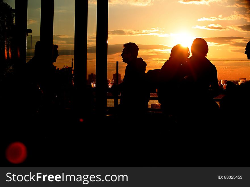 Silhouettes of patrons at a bar sitting out of doors chatting while having a drink in the golden light of sunset. Silhouettes of patrons at a bar sitting out of doors chatting while having a drink in the golden light of sunset.