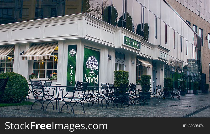White painted restaurant with the name 'Vivid' in green on the outside walls with tables and chairs on the pavement, seen after closing time and without patrons. White painted restaurant with the name 'Vivid' in green on the outside walls with tables and chairs on the pavement, seen after closing time and without patrons.