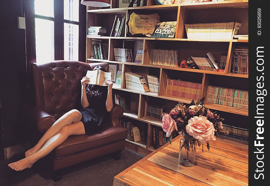 Woman in Black Mini Dress Sitting on Brown Leather Tufted Sofa Chair Beside Brown Wooden Book Shelf