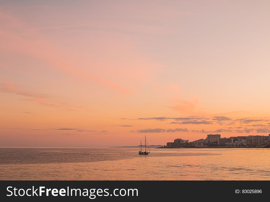 Pink skies at sunset over coastline with sailboat. Pink skies at sunset over coastline with sailboat.