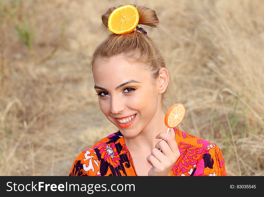 Portrait of woman outdoors in sunny field with orange slice in hair and holding orange lollipop. Portrait of woman outdoors in sunny field with orange slice in hair and holding orange lollipop.