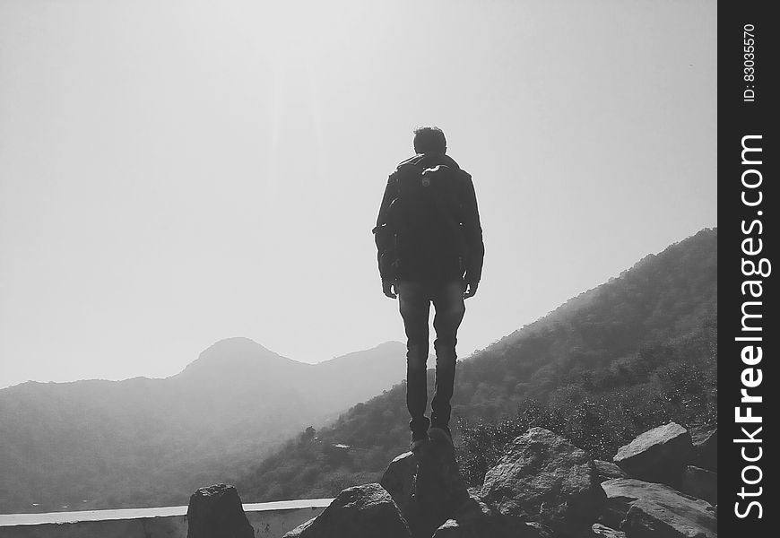 Back of man standing on boulder on mountain side with fog in black and white. Back of man standing on boulder on mountain side with fog in black and white.