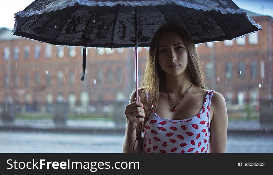 Pretty young woman under an umbrella in the rain with urban buildings in background. Pretty young woman under an umbrella in the rain with urban buildings in background.