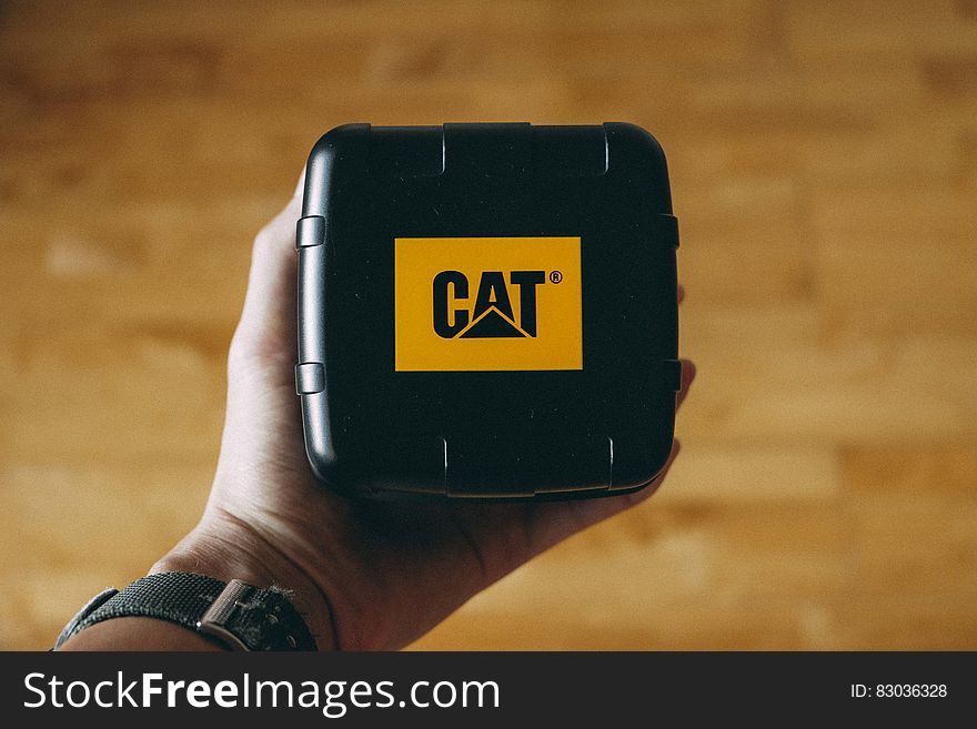 A close up of a hand holding a black box with Caterpillar company logo. A close up of a hand holding a black box with Caterpillar company logo.