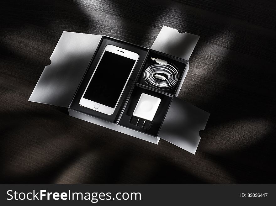Open box with new smartphone and accessories on desktop in black and white.