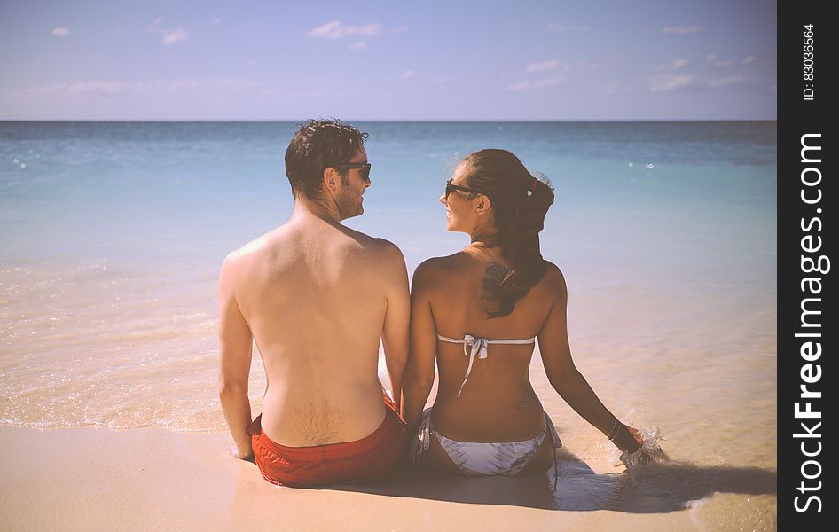 A happy couple sitting on a sandy beach looking at each other. A happy couple sitting on a sandy beach looking at each other.