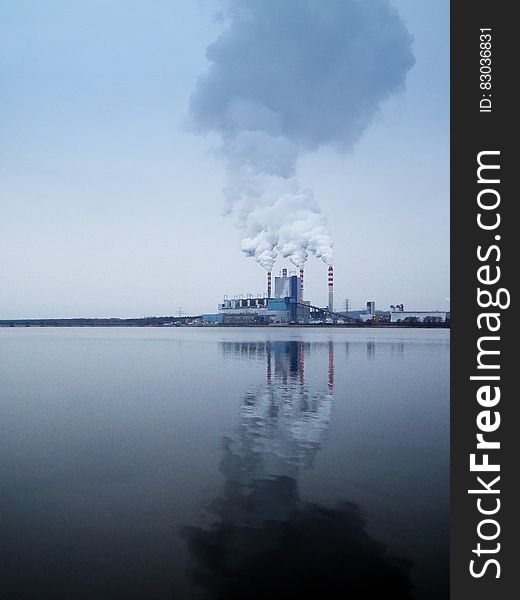 Smoke from factory stacks reflecting in water along shoreline. Smoke from factory stacks reflecting in water along shoreline.