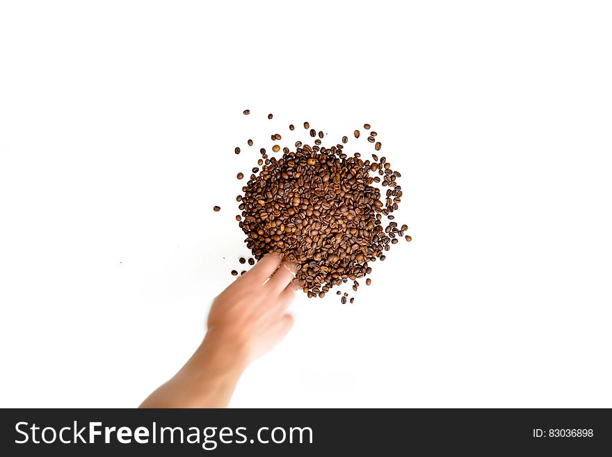 A pile of coffee beans on a white background and a hand reaching for it.