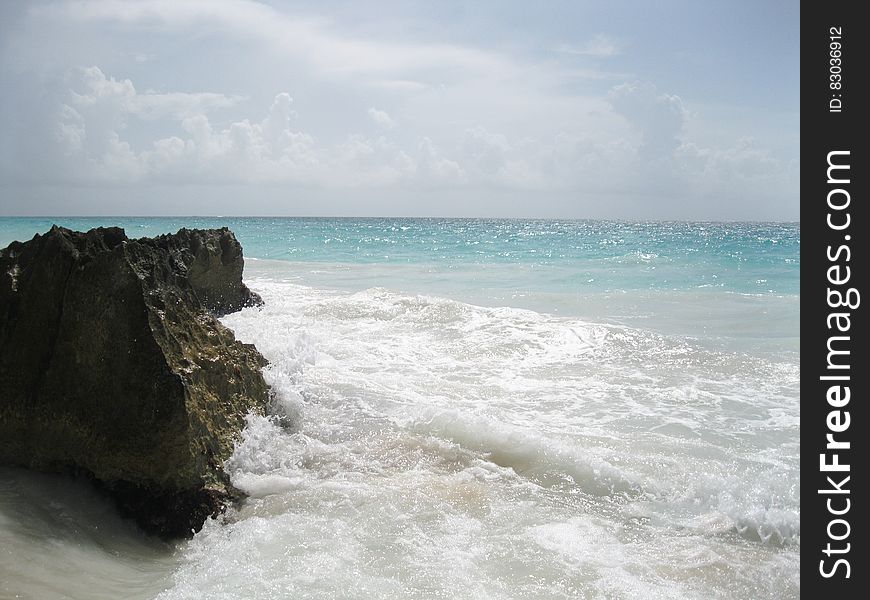A sharp rock on a sandy beach and the sea splashing against it. A sharp rock on a sandy beach and the sea splashing against it.