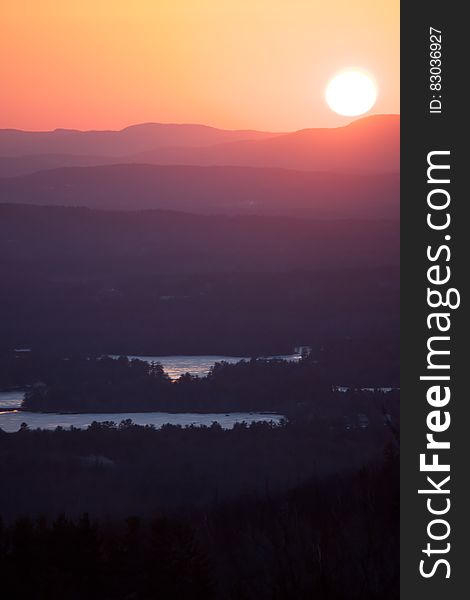 A sunrise seen over the landscape with dark forests, lakes and mountains in the distance. A sunrise seen over the landscape with dark forests, lakes and mountains in the distance.