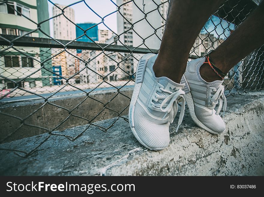 Person Wearing White Adidas Low Top Shoe Near Gray Cyclone Fence