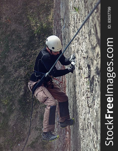 Man in harness using ropes to ascent rock face on sunny day. Man in harness using ropes to ascent rock face on sunny day.